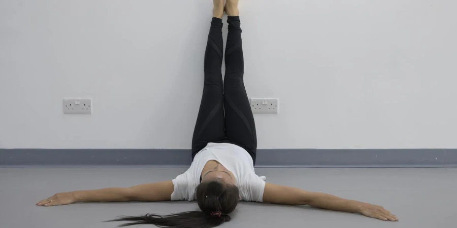 Yoga-Frau legt die Füße hoch und entspannt sich auf dem Wandhintergrund
