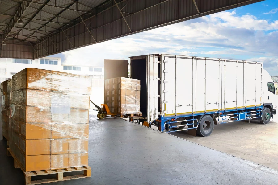 Caminhões de contêineres estacionados carregando paletes de caixas de pacotes na doca do armazém.