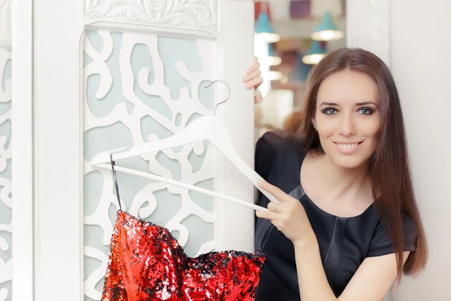 Modaya uygun bir giysiyle elbise askısını tutan gülümseyen moda