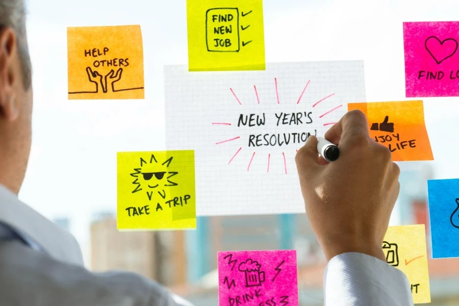 Caucasian man is looking at multicolored notes about new year resolutions.