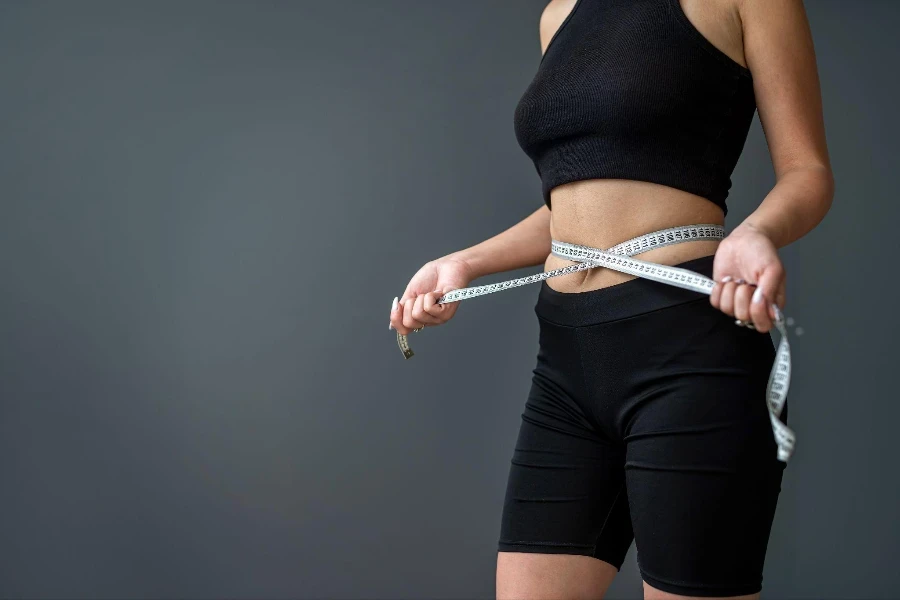 A young smiling woman measures her ideal waist with a tape