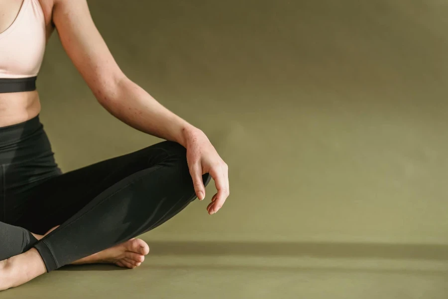 Crop unrecognizable slim female in sportswear sitting on floor and stretching legs while doing yoga in studio