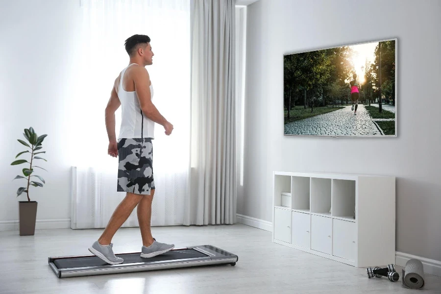 Homme sportif s'entraînant sur un tapis roulant et regardant la télévision à la maison