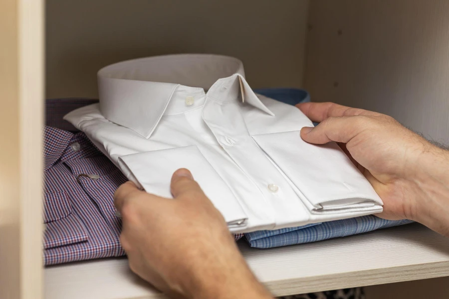 A man puts a new folded long sleeve white shirt in an open shelf