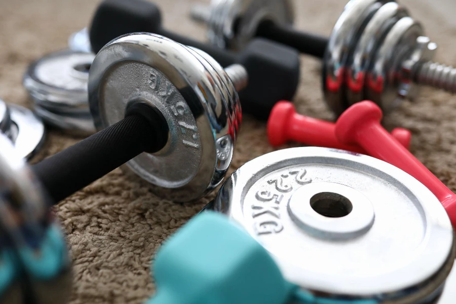 pile of shiny chrome dumbbells disks lying around grip at home rug as domestic sport exercises