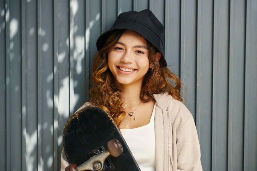 Retrato de niña feliz con sombrero de cubo sosteniendo patineta