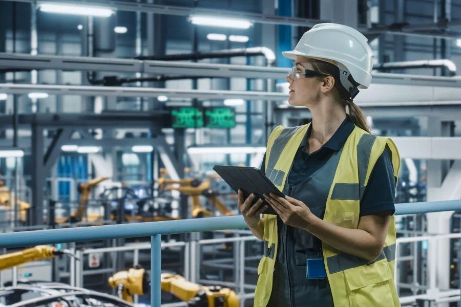 Female Car Factory Engineer in High Visibility Vest Using Tablet Computer.