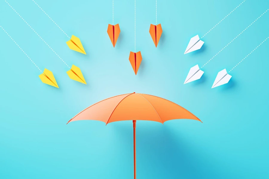 Paper planes flying towards a coral colored umbrella on blue background.