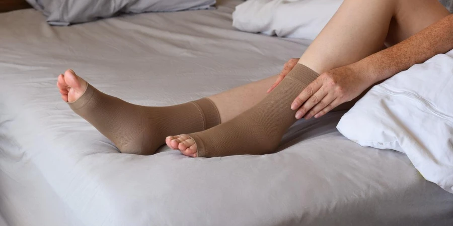 Woman sitting on top of bed putting on toeless compression socks on her legs
