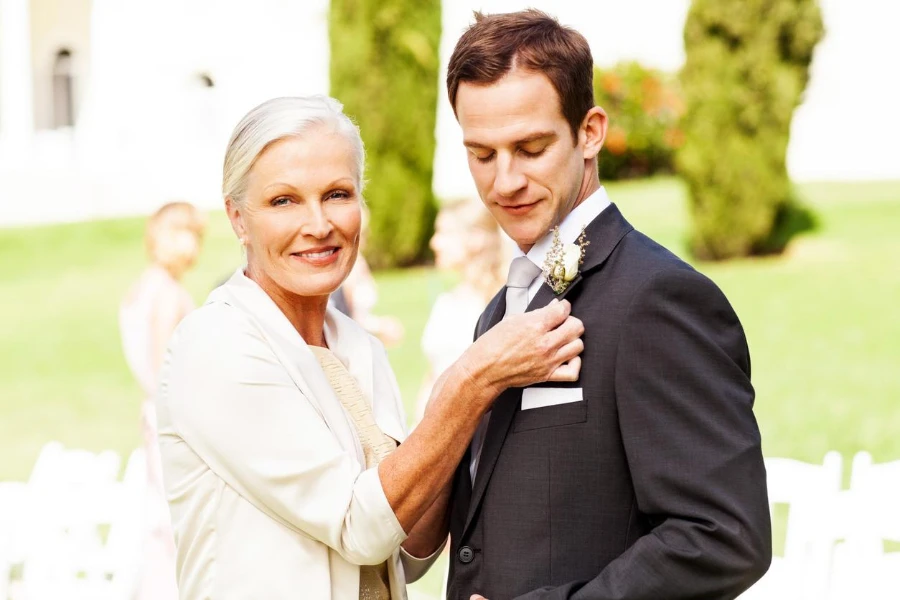 portrait of happy mother pinning corsage on groom's suit