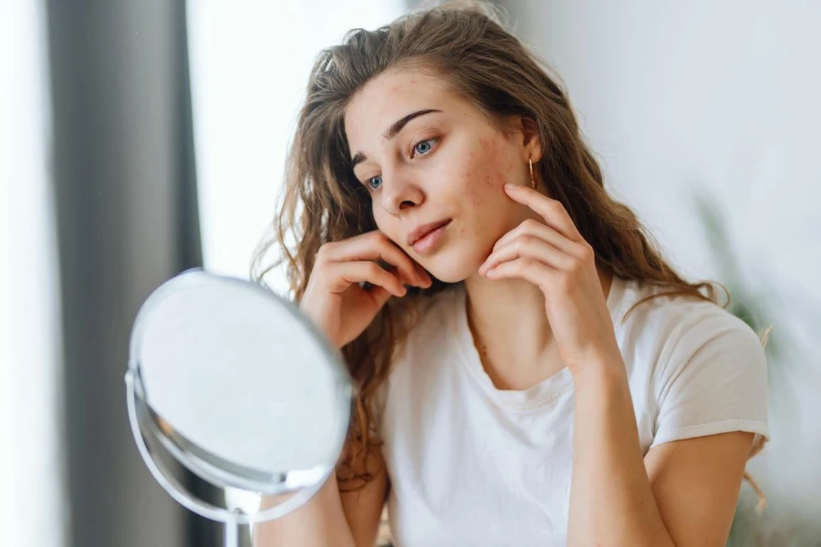 Young woman with problem skin looking into mirror