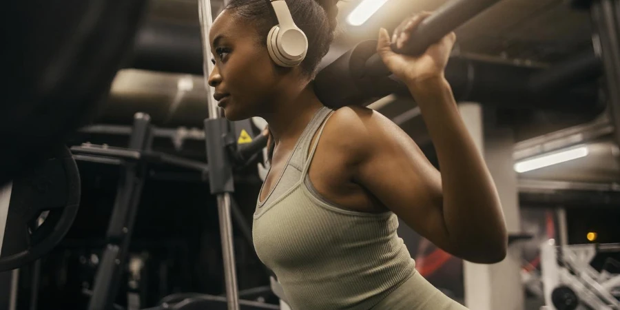 A sportswoman with headphones doing workout on smith machine
