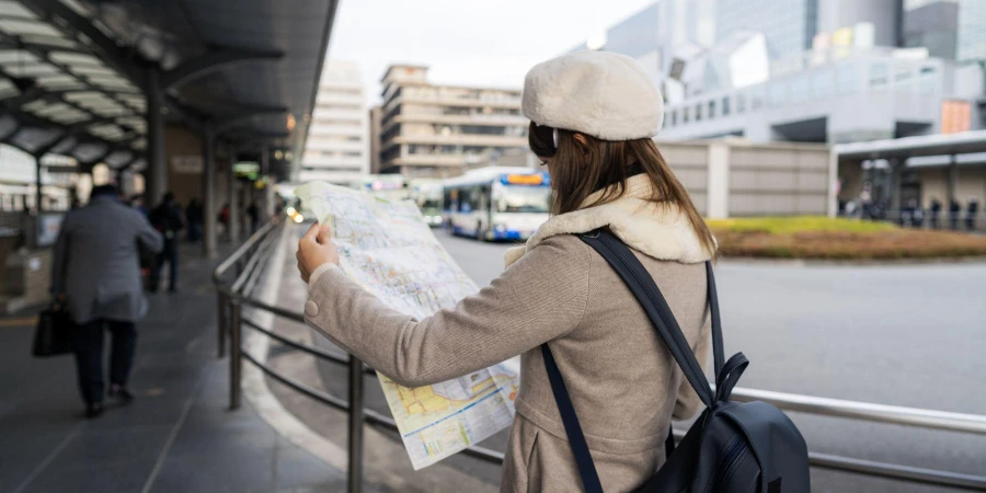 Wanita turis muda berdiri membaca peta bus di halte bus