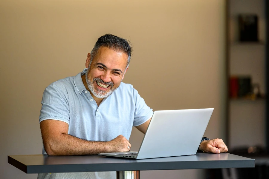 Portrait of a happy mature businessman standing at a table working at his laptop looking at camera