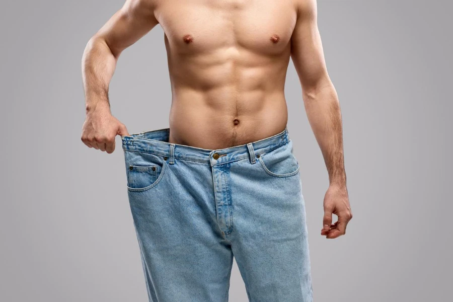 Anonymous shirtless male with muscular torso pulling huge jeans