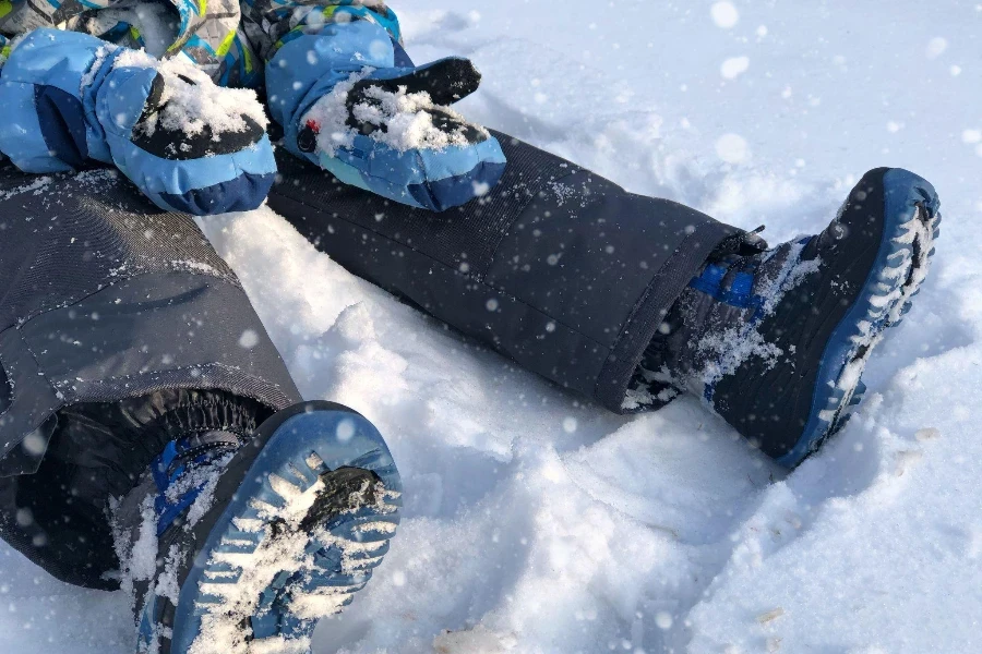 A young boy dressed in snowsuit holds snow in his gloves