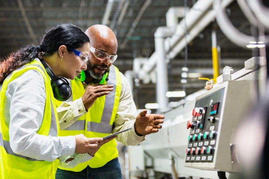 Two multi-ethnic workers working in a plastics factory, standing on the factory floor