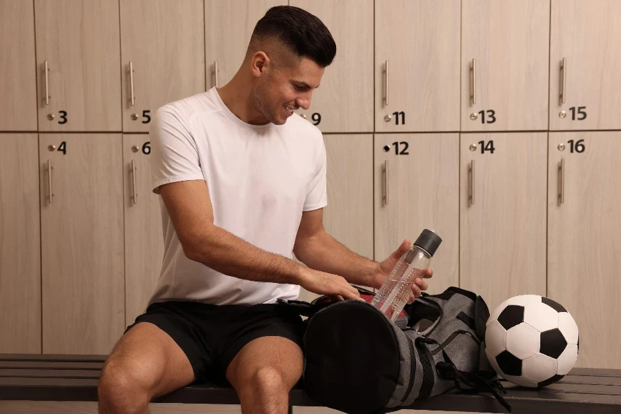 Un hombre guapo tomando una botella de una bolsa deportiva en el vestuario