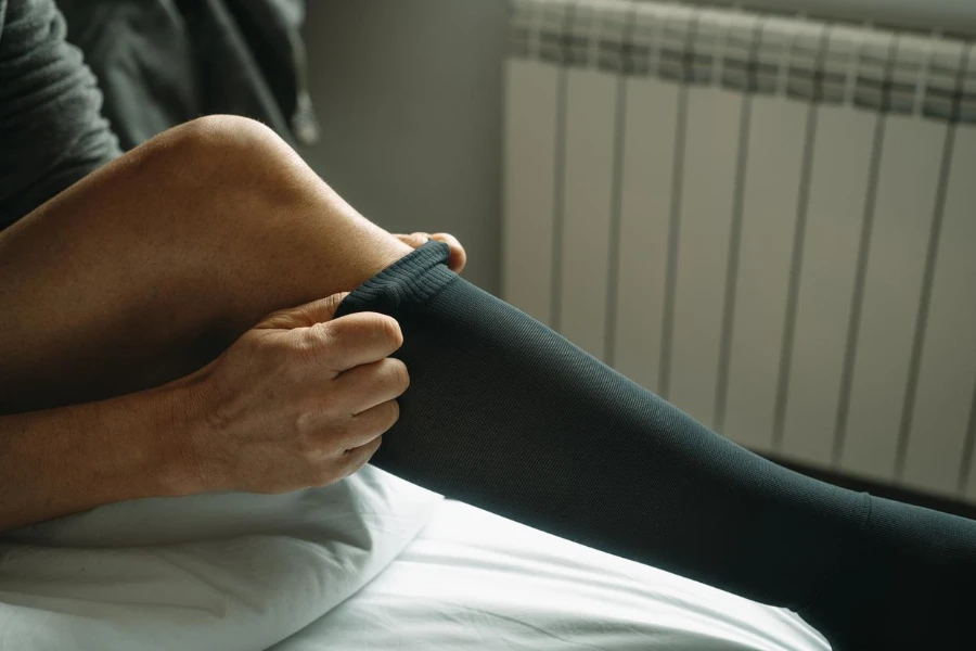 closeup of a man putting on a compression sock sitting on the bed at home