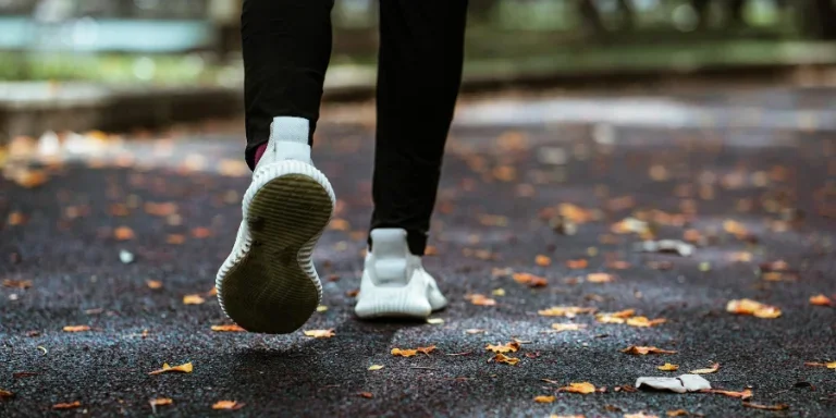 Legs of anonymous person in white sneakers and black leggings running on sidewalk