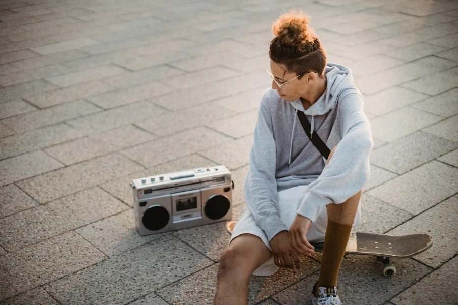 Ethnic male skater sitting on skateboard near retro boombox