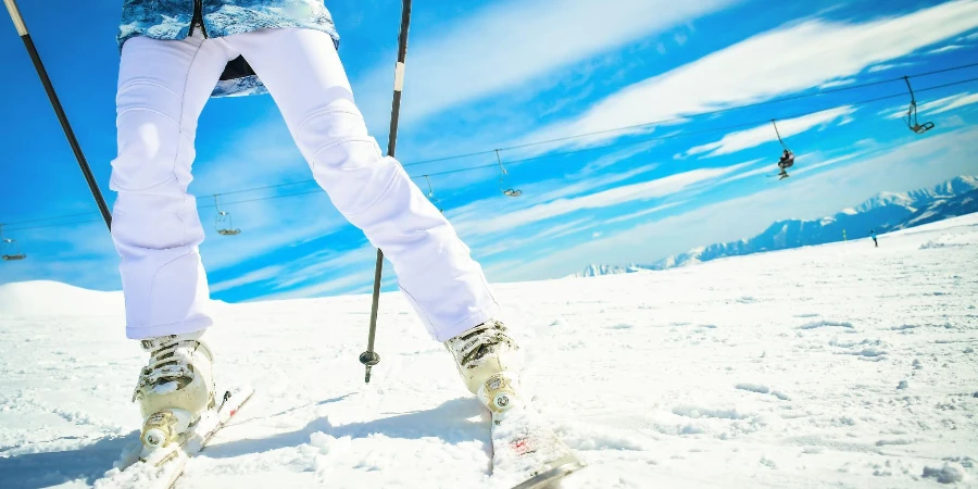 Feche a mulher esquiadora com vista inferior brilhante de botas de esqui e esquis enquanto para na escultura em movimento rápido
