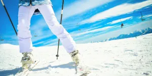 Cerrar mujer esquiadora vista inferior brillante de botas de esquí y esquís mientras se detiene en tallar en cámara rápida