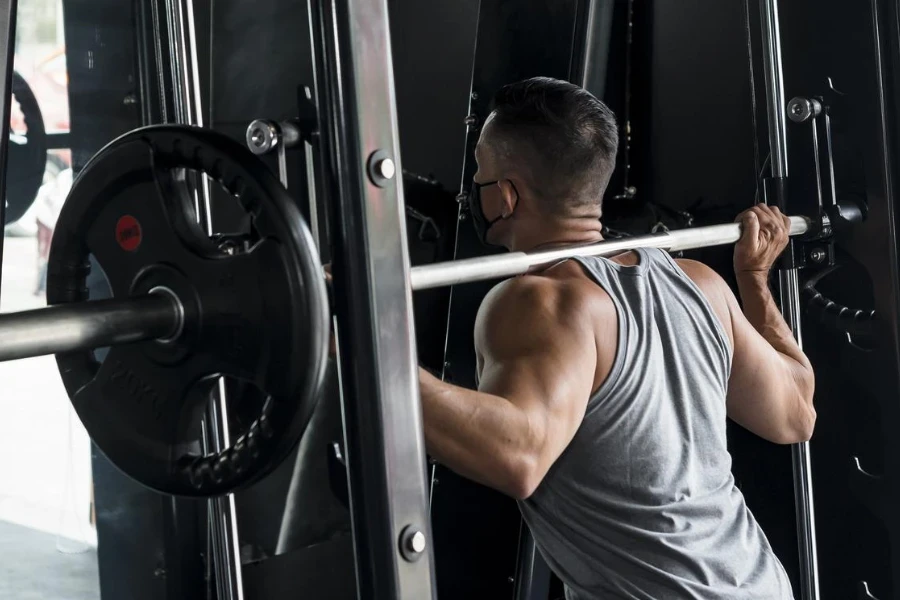 A fit Asian man performs some squats at the smith machine