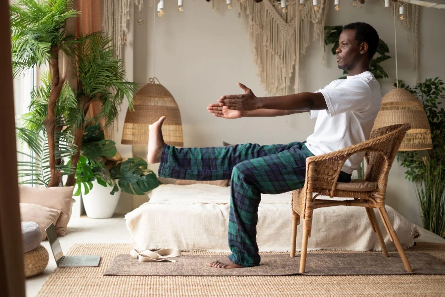 Afrikalı genç adam evindeki oturma odasında sandalye kullanarak yeni başlayanlar için yoga asanaları yapıyor