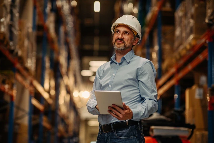 Manager con casco di sicurezza che tiene tablet digitale in magazzino