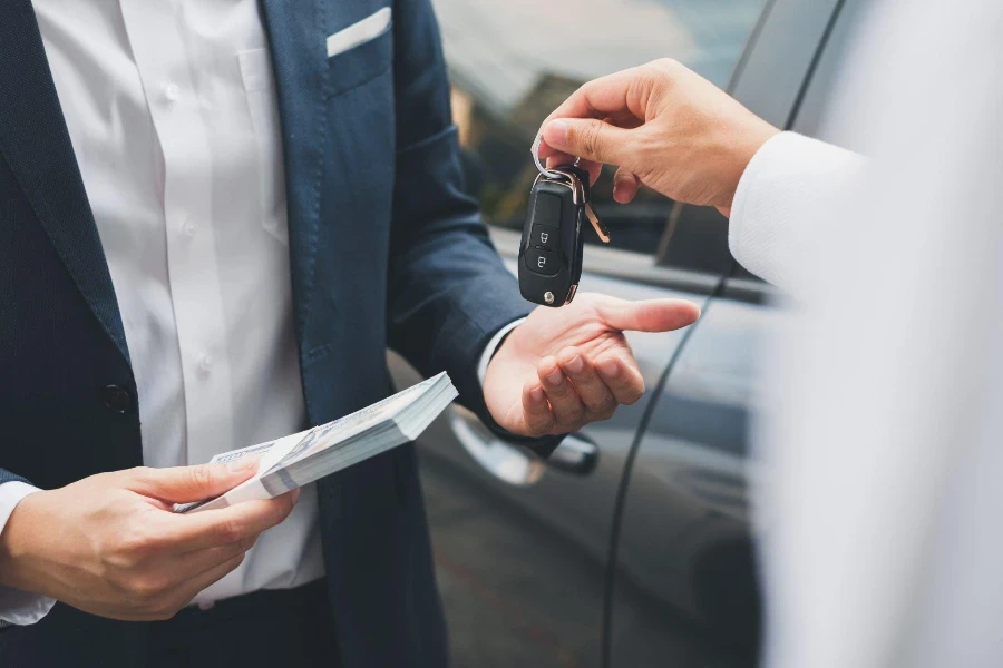 Closeup hand giving a car key and money for loan credit financial