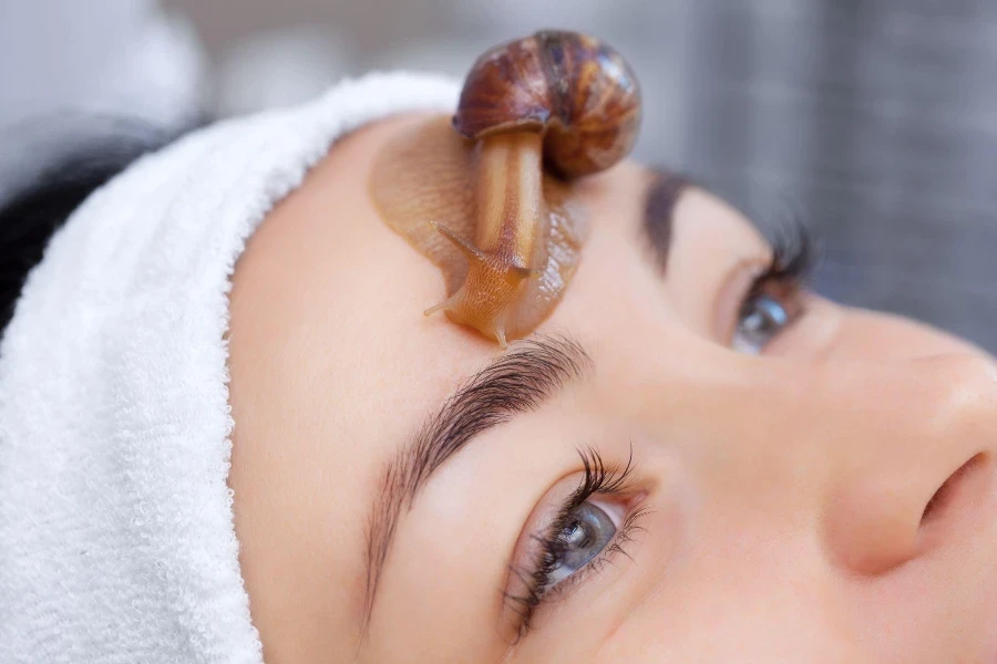 Belle jeune femme avec un escargot ahatin sur son visage