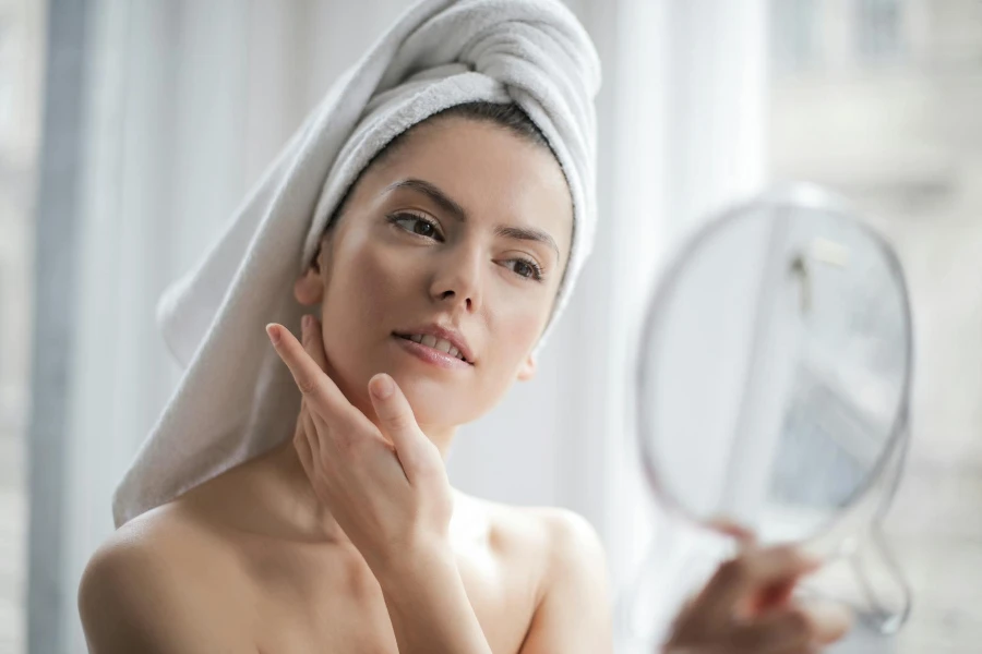 Mulher com uma toalha na cabeça olhando no espelho