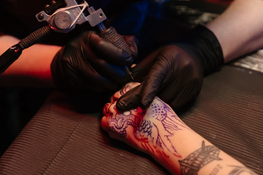 Pria menggunakan mesin tato dengan sarung tangan hitam