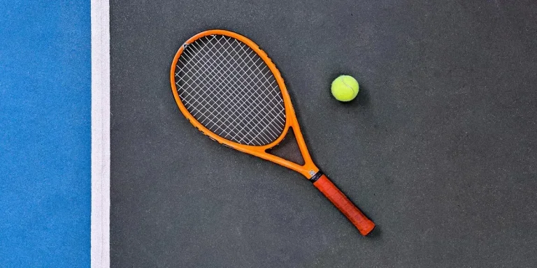 orange tennis racket beside green tennis ball