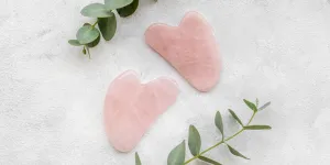 Two pink gua sha next to green leaves