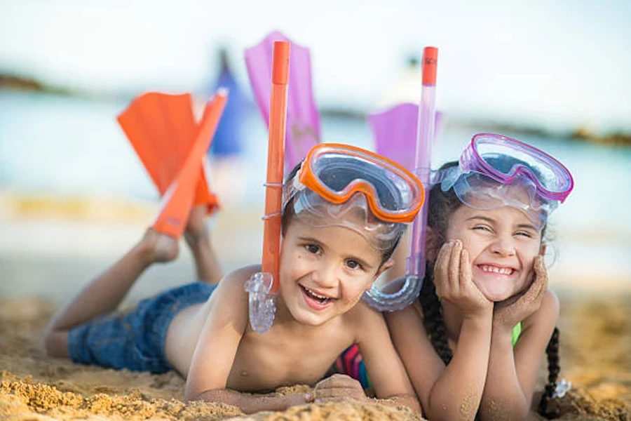 2 children laying in sand wearing snorkeling masks