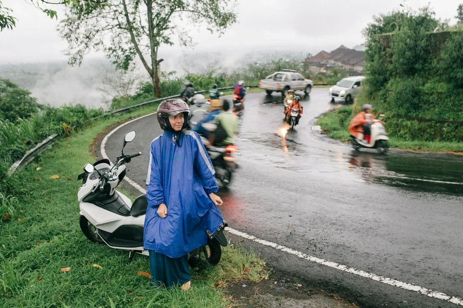 A Woman in Raincoat Sitting on a Motorcycle Beside the Road