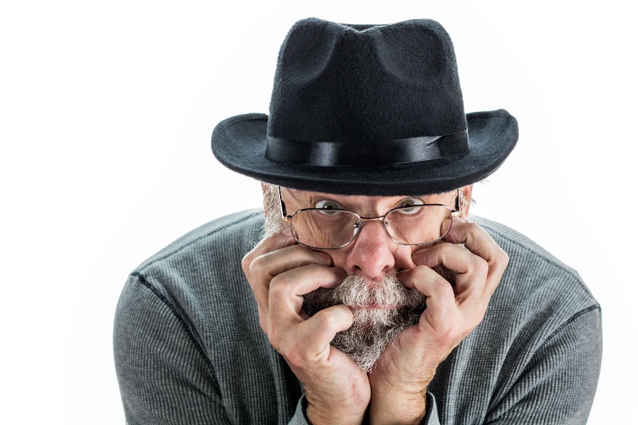 A curious senior adult man wearing a black fedora hat 