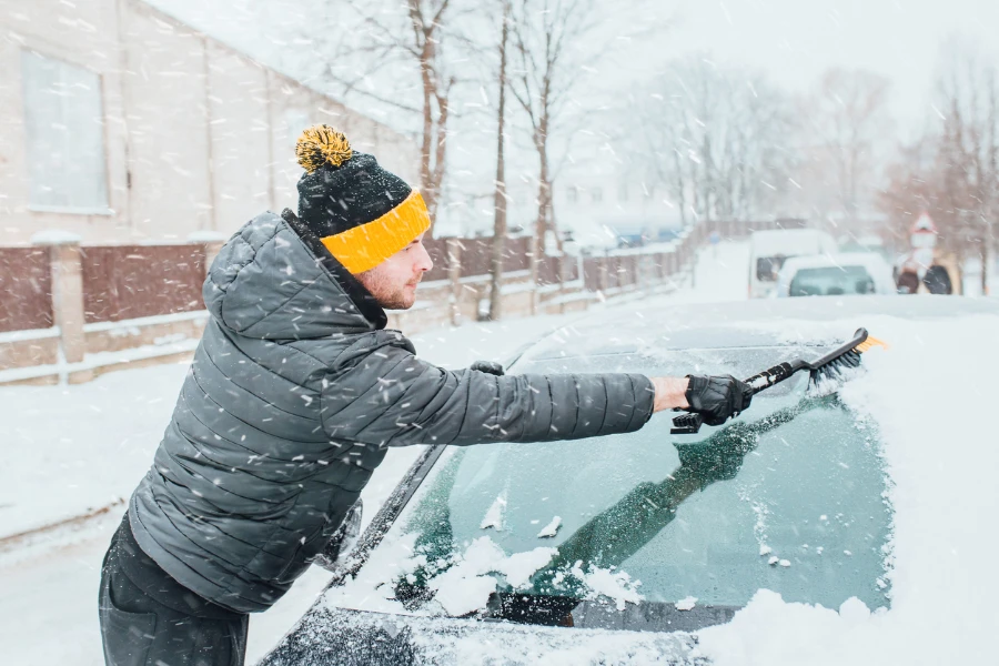 A man brushing a car brush from snow in winter in the morning