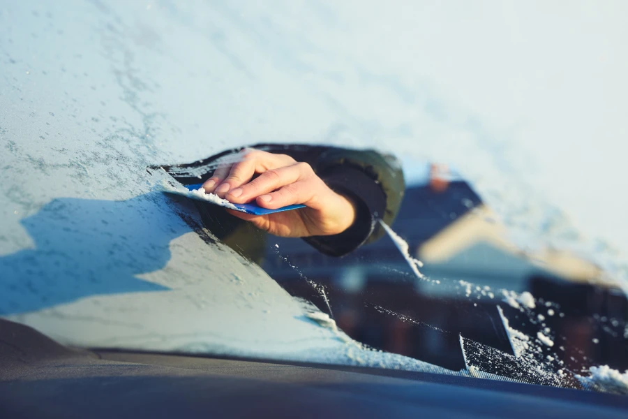 A man scratches the front window of his car on a cold winter morning