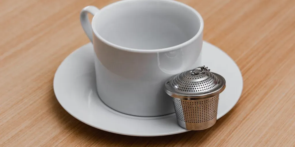 A tea infuser on a white saucer next to a cup