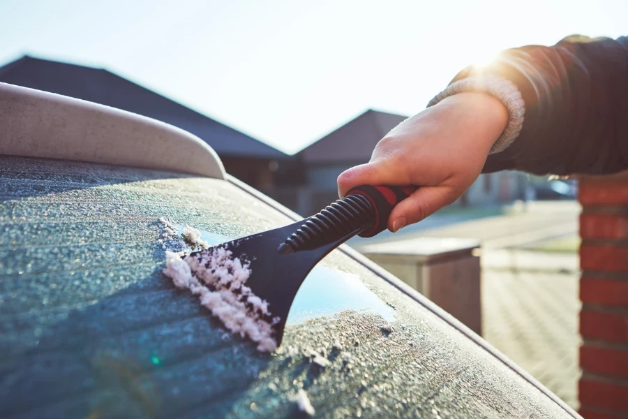 A woman scrapes frost off the front window of her car in winter