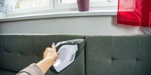 A woman using a handheld vacuum on a sofa