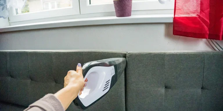 A woman using a handheld vacuum on a sofa