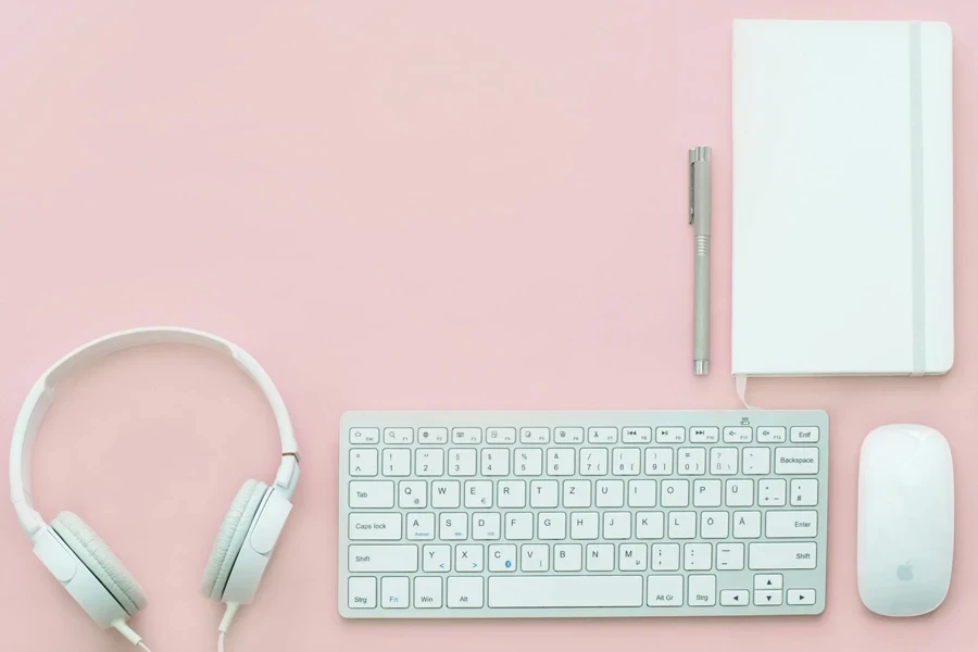 Apple Compact Keyboard, Magic Mouse, and Corded Headphones on Pink Surface