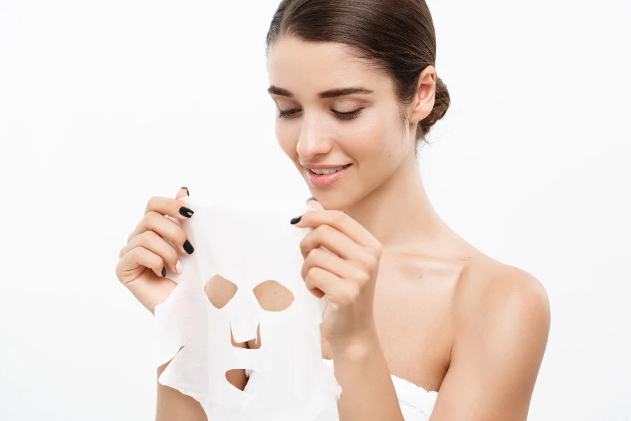 Beautiful Caucasian Woman applying paper sheet mask on her face white background