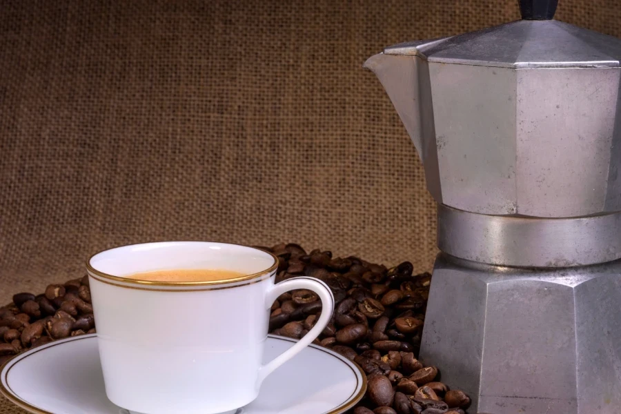 Coffee percolator beside a teacup and coffee beans