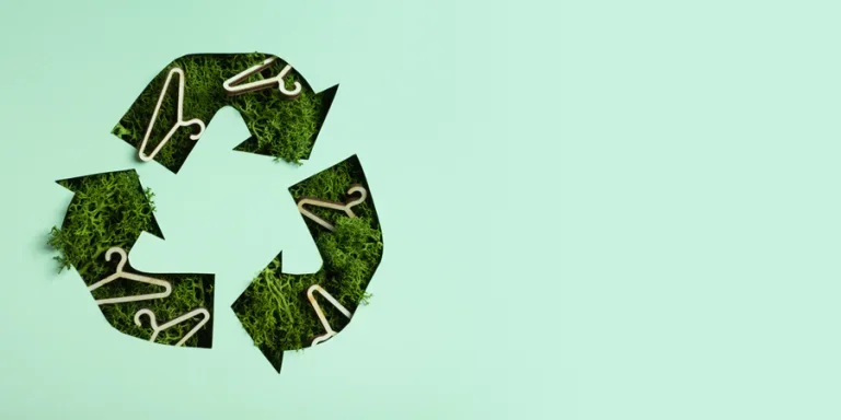 Green moss and hangers under paper cut recycling symbol. Fast fashion, slow fashion, recycling cloth concept