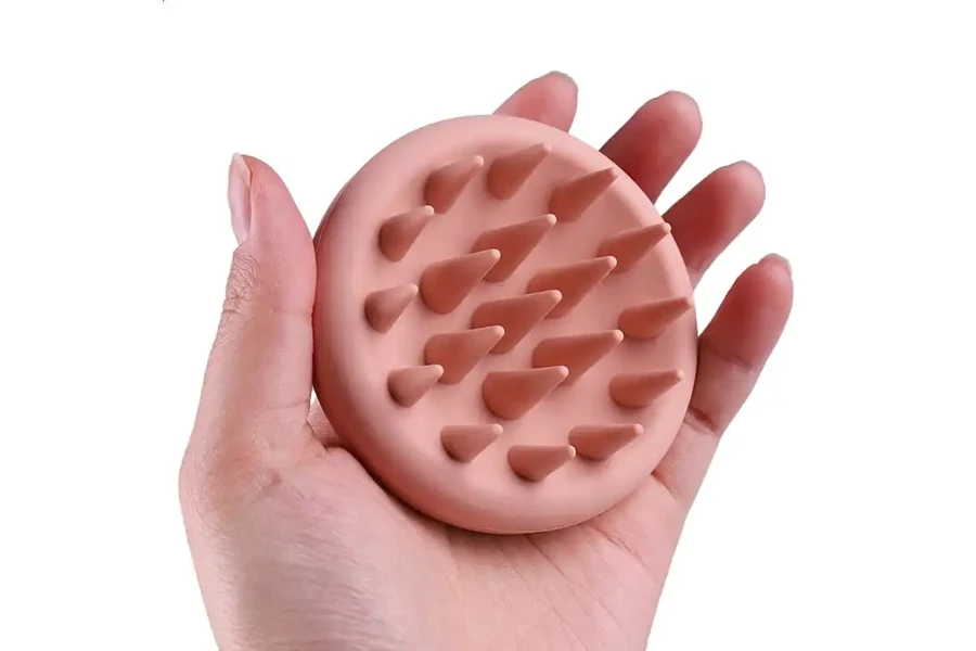 Hand holding a palm-sized manual scalp head massager